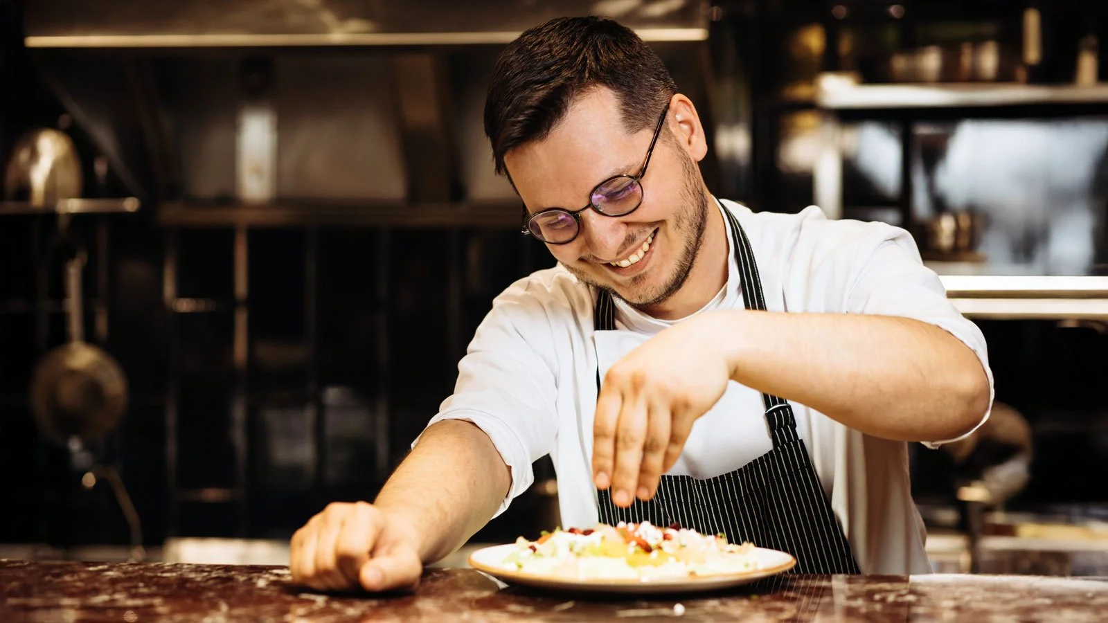 Man chef at the kitchen sprinkles sald from cabbage with pomegranate