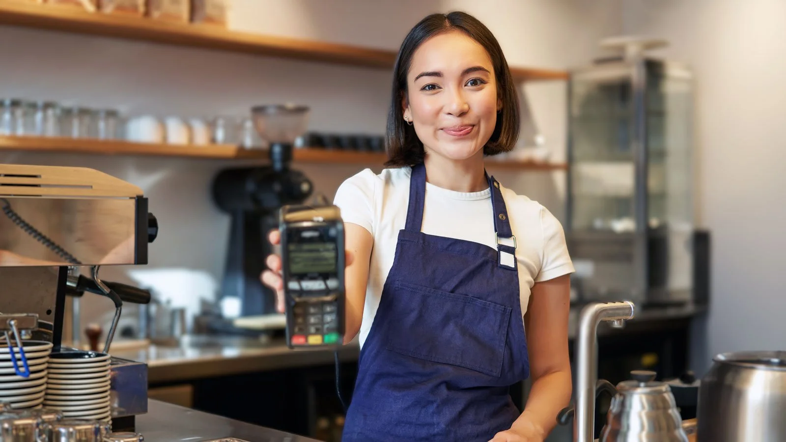 Smiling asian barista coffee shop staff gives you credit card machine