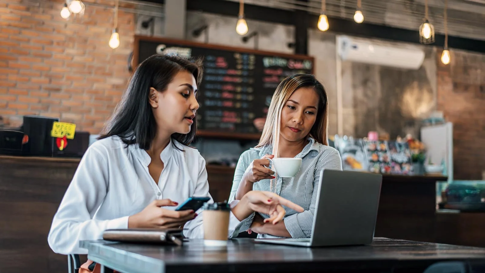 Two women sitting and working with a laptop in a coffee shop