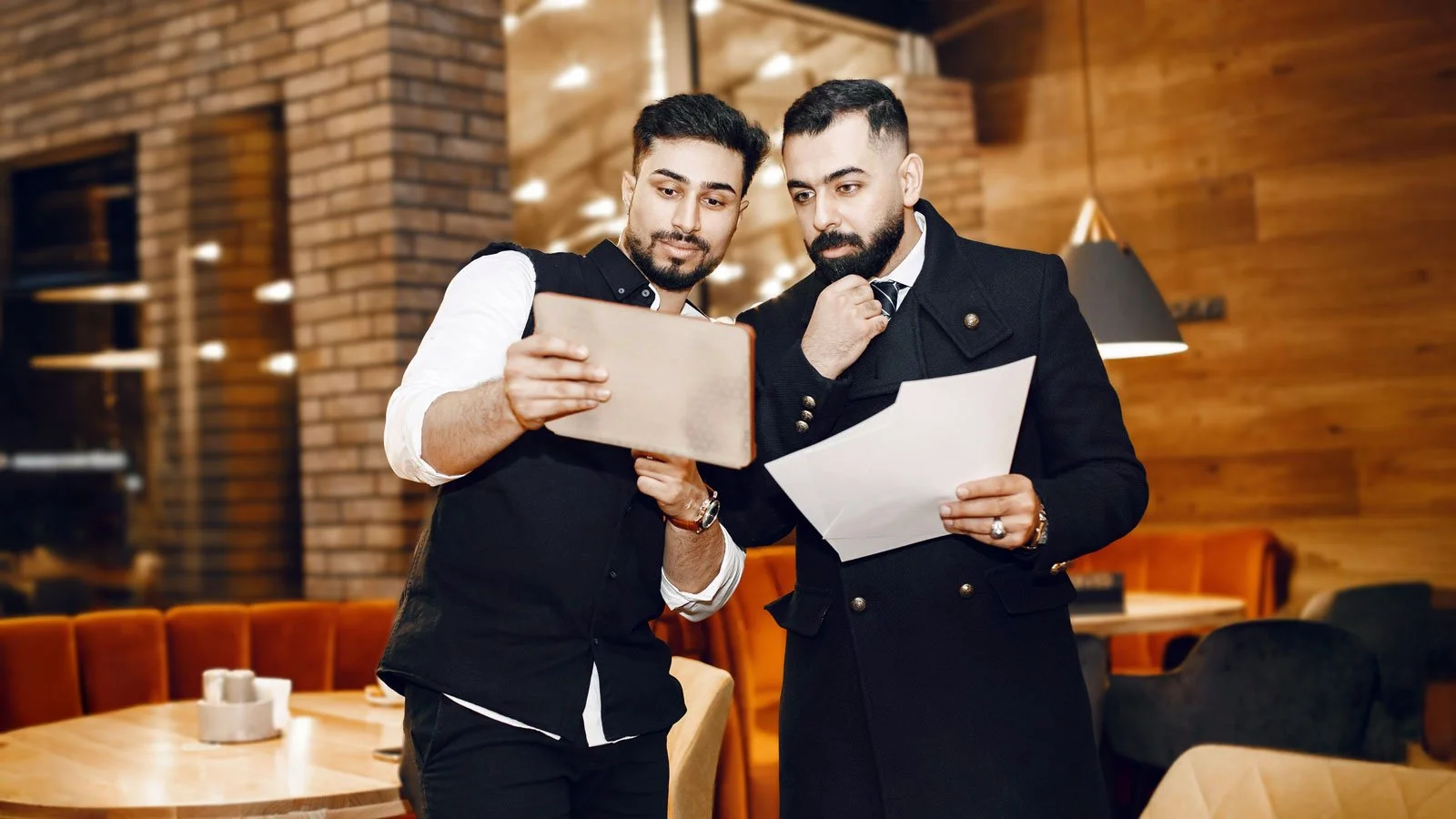 Businessmen Looking on Tablet and Documents in Restaurant
